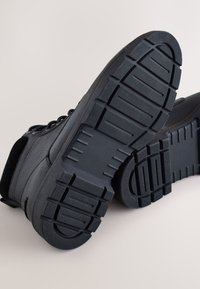 Čierne športové topánky s textúrovanou gumovou podrážkou s hlbokým vzorom, syntetickým zvrškom a pevnou šnurovacou konštrukciou.