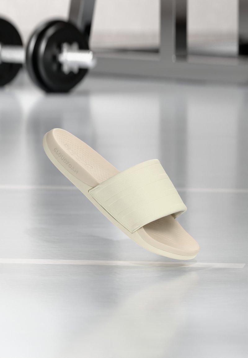 Sandalia tipo slide de color beige claro con una correa ancha y texturizada. Cuenta con una plantilla acolchada y un diseño minimalista, adecuada para uso casual.