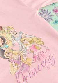 Vaaleanpunainen vaate, jossa on piirrosprinsessoja ja brodeerattu "Prinsessa"-teksti pastelliväreissä, sileä pinta ja pyöreä pääntie.