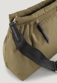 La borsa a spalla imbottita verde oliva presenta due scomparti con zip e una tracolla nera regolabile con una superficie texturizzata.