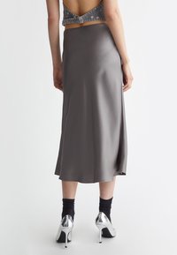 Gonna di satin grigia a media lunghezza con una texture liscia, indossata con un top in denim senza schienale e decollete argentati con tacco a spillo, che mostrano un design minimalista.