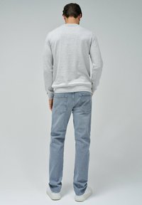 Grauer Sweatshirt mit langen Ärmeln und Rundhalsausschnitt, kombiniert mit hellblauen Jeans mit einem verblassten Muster und Gesäßtaschen. Weiße Sneaker.