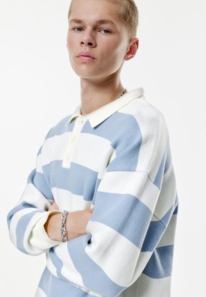 Gestreepte collared trui in lichtblauw en wit, met een textuurgebreide stof, een placket met vier knopen en geribbelde manchetten. Armband zichtbaar om de pols.