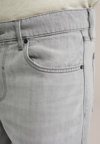 Grijze denim jeans met een close-up van de taille, met een voorzak, eenvoudige stiksels en een subtiele textuur.