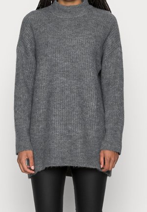 Lang grå strikket sweater med høj hals båret over sorte læderbukser, vist fra nakke til midt på låret.