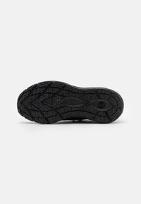 Suela de zapatilla deportiva negra con un patrón de textura en la suela y el logo de Under Armour en el centro, mostrada sobre un fondo blanco.