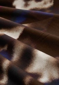 Bruine, zwarte en witte zachte stof met een vage, abstracte patroon, getoond in close-up plooien en textuur.
