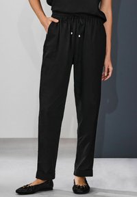 Pantaloni negri, ușori, cu talie elastică și șnur, cu buzunare laterale și tivuri rulou. Textură netedă, croială ajustată.