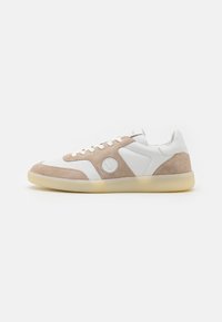White and tan sneakers featuring a suede and leather design, round emblem, and a translucent rubber sole. Subtle stitching details.