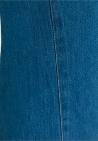 Blå denimtyg som visar en närbild av en vertikal söm med en kontrasterande brun tråd, som framhäver textur- och färgdetaljer.