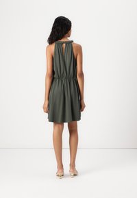 Vestido verde sem mangas com cintura elástica e detalhe de abertura nas costas. Feito de um tecido suave, cai acima dos joelhos, com um corte descontraído.