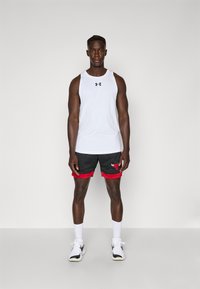 Débardeur de sport sans manches blanc avec un logo noir, associé à un short en maille noir avec des accents rouges et un logo, complété par des baskets blanches.