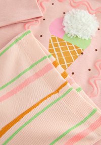 Tissu rose avec un graphique de cornet de glace orné d'accents colorés et d'un pompon texturé blanc. Rayures roses avec des lignes vertes et orange.