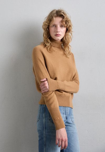 Barna garbó nyakú pulóver bordázott mandzsettával és hemivel, puha anyagból készült, világoskék farmerrel párosítva. Egyszerű dizájn, nem látható minták.