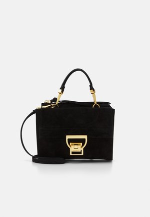 Bolso de ante negro con cierre dorado, asa superior y correa de hombro desmontable sobre fondo blanco.