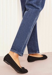 Zwarte suède ballerina's met een ronde neus, een lichte hak en een gestructureerd oppervlak, gecombineerd met cropped donkerdenim jeans.