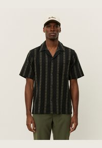 Short-sleeve black button-up shirt with vertical white stripes, a chest pocket, and a lightweight fabric. Worn with olive green trousers.