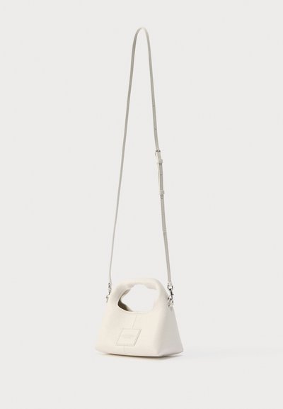 Λευκή τσάντα χειρός από υφή δέρματος, με μοναδικό σχήμα λαβής και μακρύ ρυθμιζόμενο λουρί. Διακρίνονται μικρές λεπτομέρειες με λογότυπο.