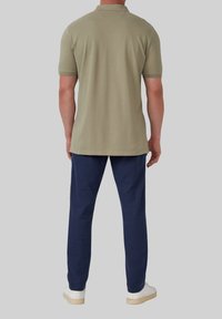 Oliwkowa koszulka polo z krótkim rękawem, w teksturowanym materiale, w zestawieniu z granatowymi spodniami i białymi trampkami, widok z tyłu.