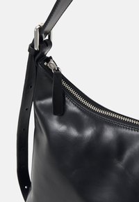 Fekete bőr válltáska állítható pánttal és ezüst cipzáras zárással, sima fehér háttér előtt bemutatva.
