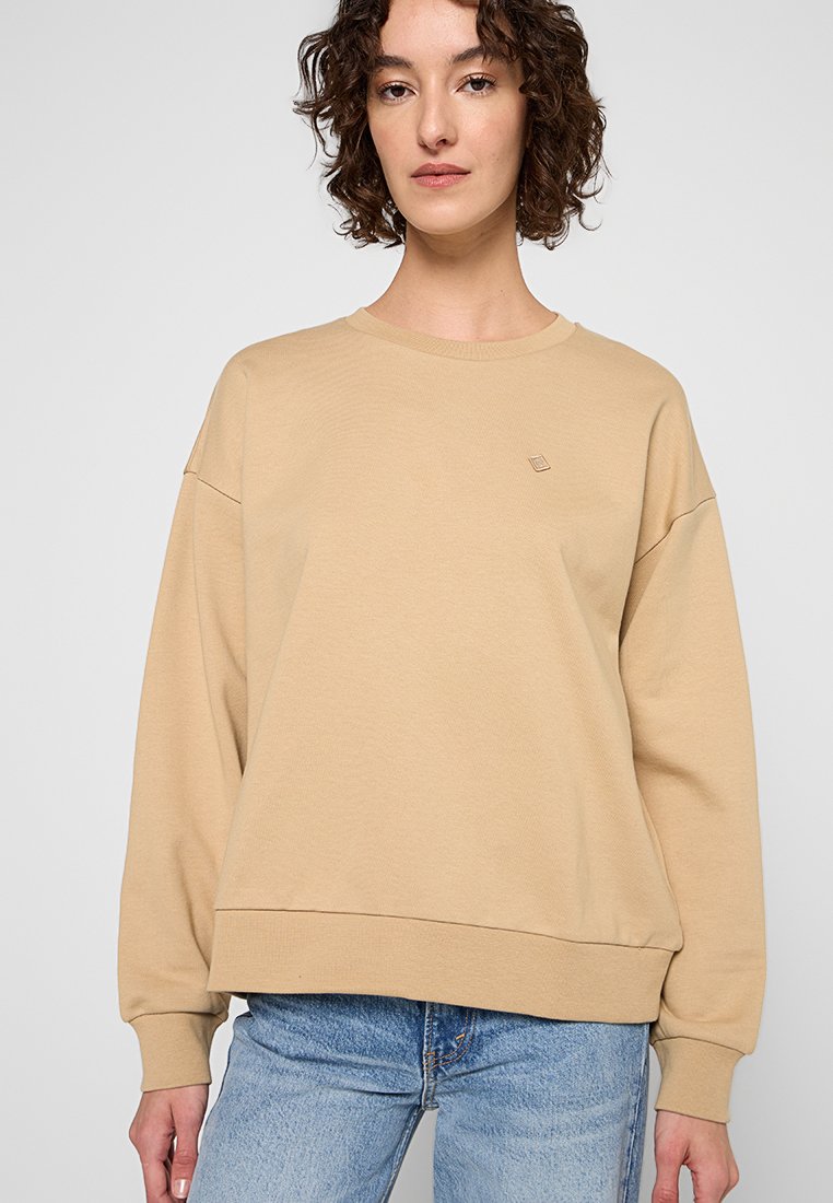 Sudadera beige con cuello redondo, hombros caídos y bajo acanalado. Tejido suave con un sutil detalle de logo en el pecho.