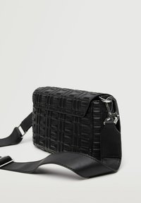 Bolso cruzado negro texturizado con una superficie estampada, cierre a presión magnético y correa ajustable. Los acentos de hardware plateado complementan el diseño.