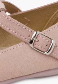 Zapato de ante rosa con correa entrecruzada y detalle de hebilla plateada. Presenta un forro interior suave y un diseño de punta redondeada.