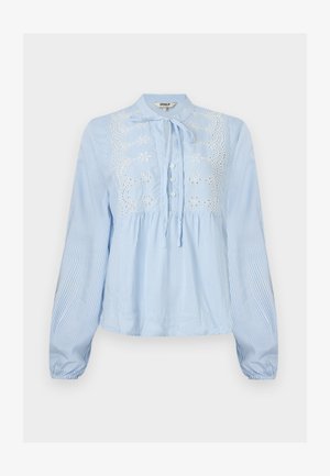 Lyseblå bluse med lange ermer og hvite vertikale striper, knappestolpe foran, knytebånd i halsen, og hvit blomsterbroderi på brystet.