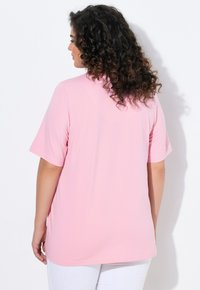 Top rosa a maniche corte con vestibilità comoda, realizzato in tessuto morbido. Presenta un colletto rotondo e un orlo posteriore leggermente più lungo.
