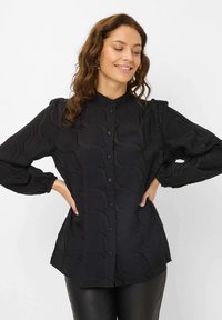 Black button-up shirt with a textured wave pattern, featuring long puff sleeves and a curved hemline, made from lightweight fabric.