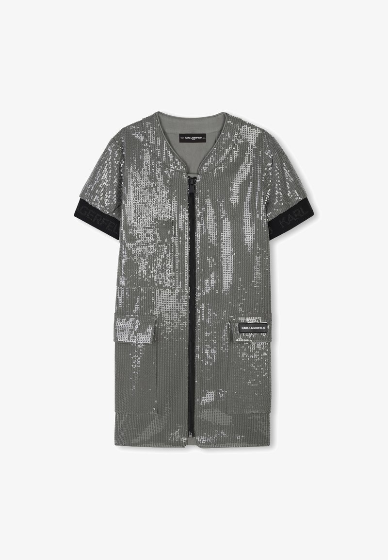 Robe en sequins argentés avec des manches courtes, fermeture éclair et deux poches sur le devant. Présente une texture côtelée et une bande logo noire au niveau des manches.