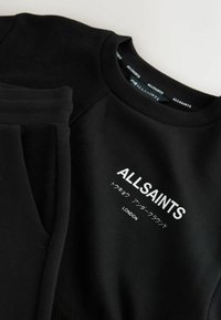 Svart sweatshirt med texturerade ärmar, ribbad halsringning och en framträdande vit logotyp med japansk text. Mjuk tyg med en slät yta.
