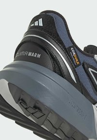 Laufschuh für Herren in einem Schwarz-Grau-Farbschema, aus Cordura-Stoff, mit grauem gepolstertem Zwischensohl und strukturiertem Gummisohle.