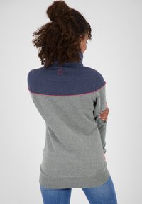 Maglione grigio e blu navy con colletto alto, caratterizzato da dettagli in cucitura rosa e un logo circolare sul retro. Tessuto morbido con vestibilità comoda.