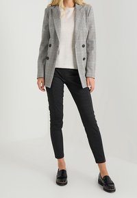 Grå plaid dobbeltradet blazer over en lys sweater, parret med sorte ternede bukser og glatte sorte loafers. Glatte teksturer.