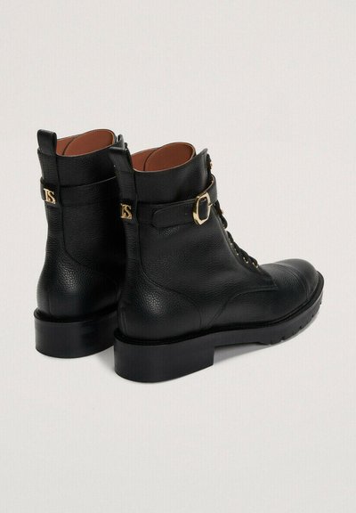 Črne usnjene gležnjarje z teksturiranim koncem, ki imajo zlat zaponko, vezalni sprednji del in debel črn podplat.