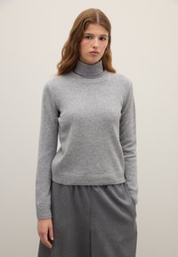 Gray turtleneck sweater made of soft knit fabric, featuring long sleeves and ribbed cuffs and hem. Worn with a gray, loose-fitting skirt.
