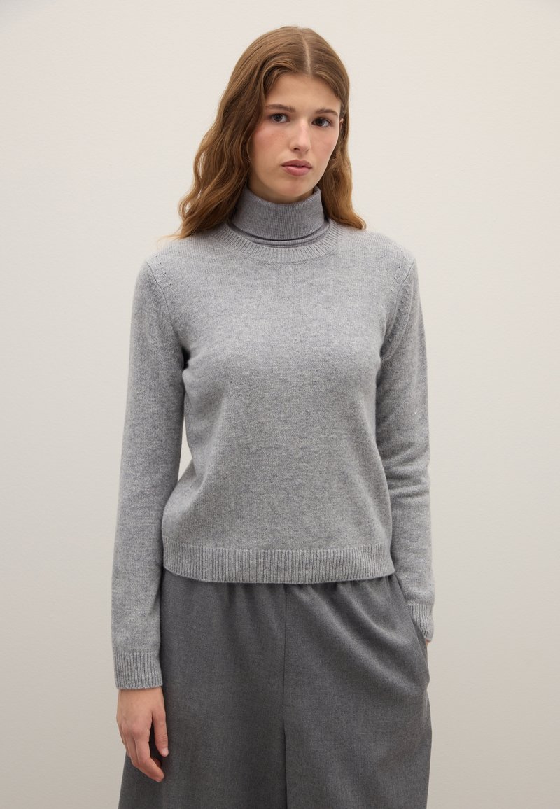Gray turtleneck sweater made of soft knit fabric, featuring long sleeves and ribbed cuffs and hem. Worn with a gray, loose-fitting skirt.
