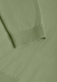 Pull en tricot vert clair avec poignets côtelés et texture lisse, mettant en valeur un gros plan de l'élasticité et du tissage du tissu.
