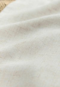 Tissu beige clair texturé avec un motif de tissage subtil, présentant des plis et des froissements pour un aspect naturel et doux.