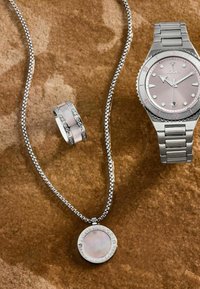 Orologio da polso argentato con quadrante rosa, collana in argento con ciondolo tondo e anello con fascia lucida e piccoli pietre.