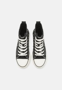 Zapatillas altas negras de lona, con cordones blancos, punteras de goma y tachuelas plateadas decorativas a lo largo de los lados.