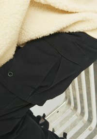 Black cargo pants feature side pockets and a smooth texture, paired with a beige fleece top showcasing a soft, fluffy material.