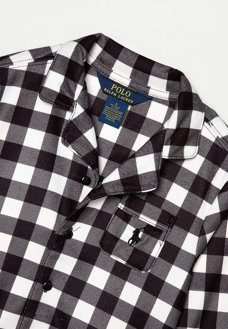 Chemise en flanelle noire et blanche à carreaux avec un design à boutons, col pointu, poche poitrine et détail de logo brodé.