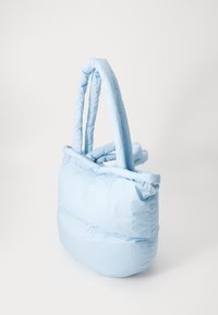 Sac fourre-tout matelassé bleu clair avec une texture douce et quiltée, des poignées arrondies, présentant un design structuré et un style minimaliste.