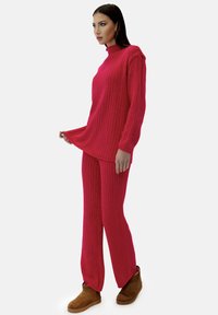 Roze geribbelde trui en bijpassende broek van zachte stof. De trui heeft een hoge hals en afgesneden schouders. Gepaard met bruine enkelboots.