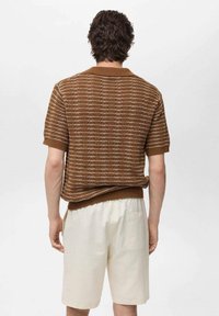 Hnědá pletená košile s krátkým rukávem a pruhovaným vzorem, s žebrovaným límečkem a manžetami; v kombinaci se smetanovými šortkami; hladká textura.