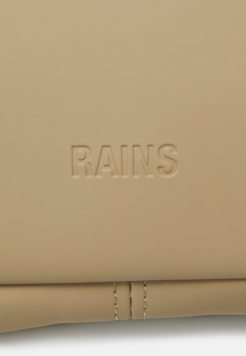 Sac beige avec texture lisse et mate. Présente le logo en relief "RAINS", un détail de couture subtil en bas et un design minimaliste.