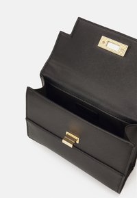 Sort tekstureret håndtaske med en struktureret form, der har en guldklipslås og et enkelt rum. Interiøret er foret, minimalistisk design.