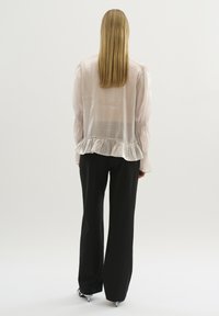 Lichtroze, doorschijnende blouse met lange, pofmouwen, smock-mouwen en een gerimpelde zoom, gecombineerd met op maat gemaakte zwarte broeken.